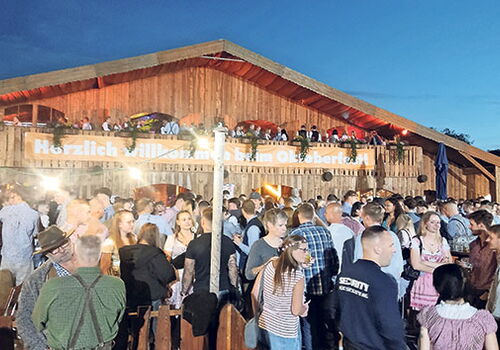Menschenmenge vor einem Holzgebäude beim Oktoberfest.