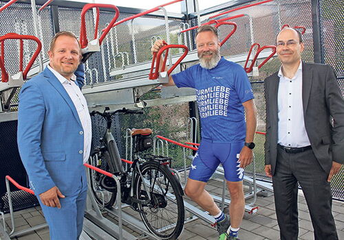 Drei Männer posieren neben einem Fahrradständer.