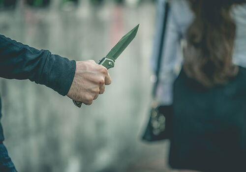 Person mit Messer in der Hand, Frau geht voraus.