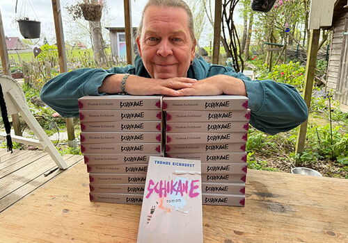 Person lehnt auf einem Tisch mit gestapelten Büchern.