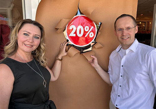 Zwei Personen neben 20%-Rabatt-Schild im Geschäftseingang.