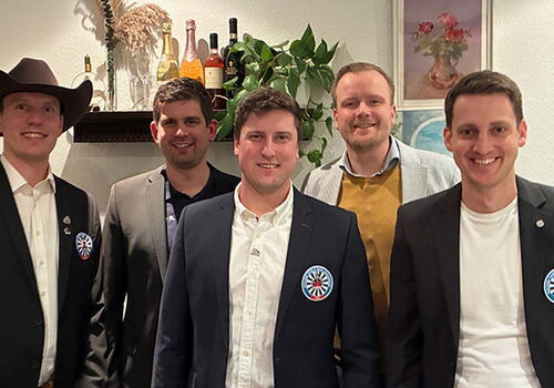 Fünf lächelnde Männer in Anzügen stehen nebeneinander.