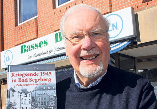 Peter Zastrow hält ein Buch vor einem Gebäude