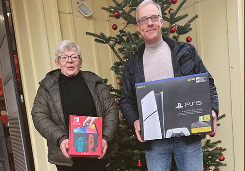 Zwei Personen mit Spielkonsolen vor einem Weihnachtsbaum.