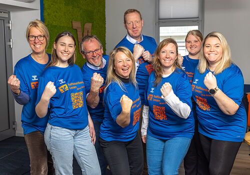 Gruppe von acht Personen in blauen T-Shirts posiert lächelnd.