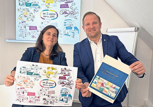 Zwei Personen halten Pläne zur Stadtentwicklung hoch.