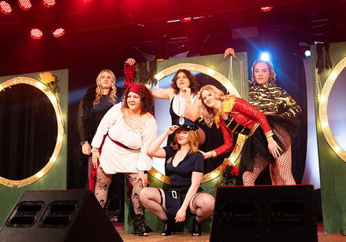 Frauen in Kostümen auf einer Bühne mit buntem Licht.