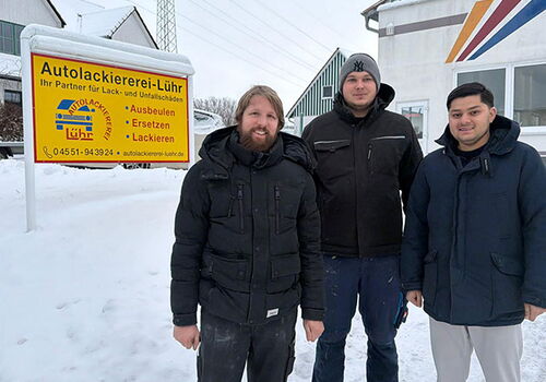 Drei Männer vor Autolackiererei-Schild im Schnee.