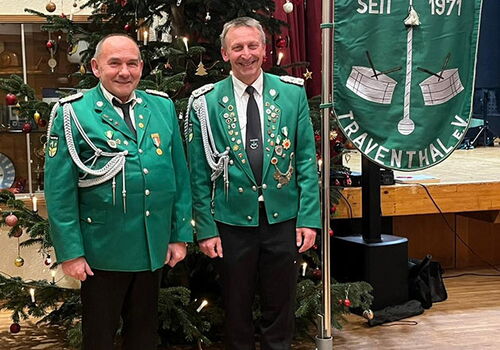 Zwei Männer in grünen Uniformen vor Weihnachtsbaum und Banner.