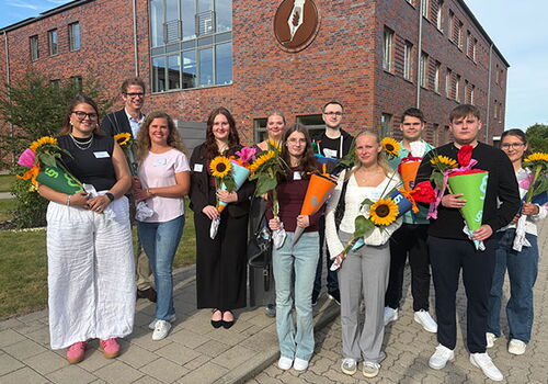 Gruppe von Studenten mit Blumensträußen vor einem Backsteingebäude