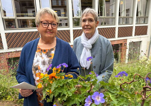 Zwei Frauen mit Blumen vor einem Gebäude.
