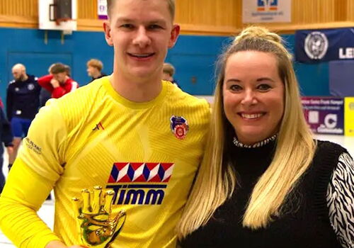 Zwei Personen mit einem Pokal in einer Sporthalle.