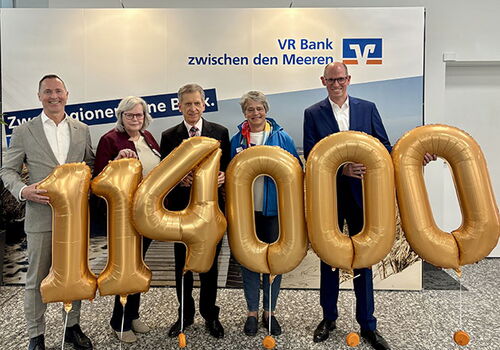 Fünf Personen halten goldene Zahlenballons: 114000.
