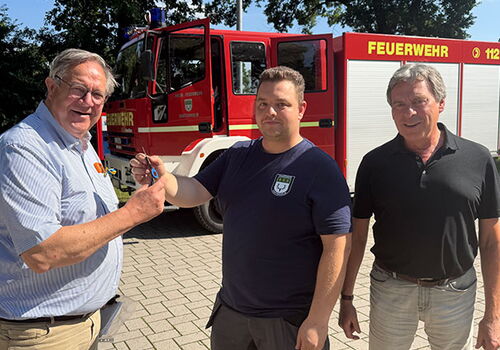 Drei Männer vor einem Feuerwehrfahrzeug bei der Schlüsselübergabe