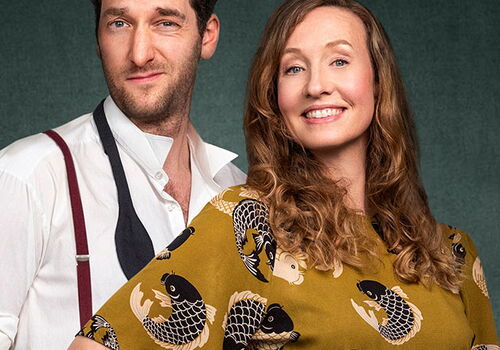 Ein Mann und eine Frau lächeln vor grünem Hintergrund.