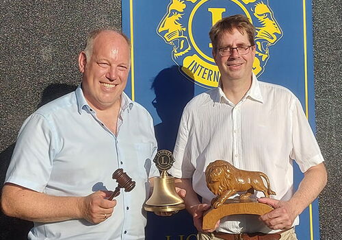 Zwei Männer mit Objekten vor einem Lions Club Banner.
