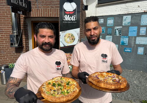 Zwei Männer halten Pizzen vor einem Restaurant.