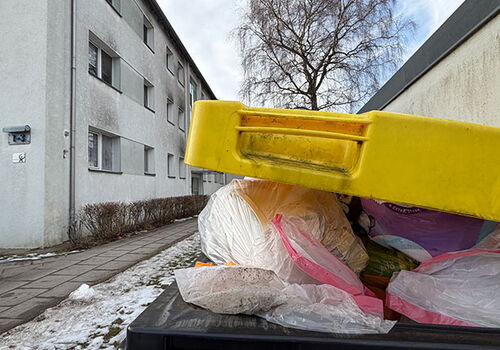 Mülltonne mit gelbem Deckel in verschneiter Straße.