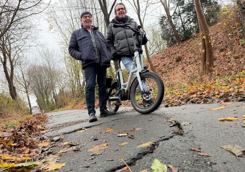 Zwei Männer posieren mit Fahrrad auf herbstlichem Weg.