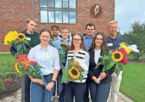 Gruppe von Menschen hält Blumensträuße vor Gebäude.