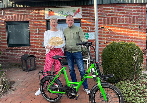 Ein Paar mit Kuchen und grünem Fahrrad vor einem Gebäude.