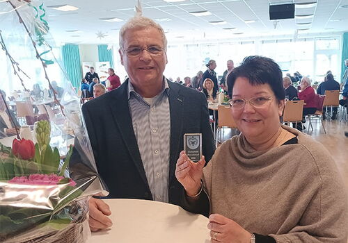 Zwei Personen halten eine Medaille in einem vollen Raum.
