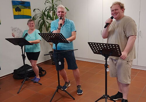 Drei Personen singen mit Mikrofonen und Notenständern.
