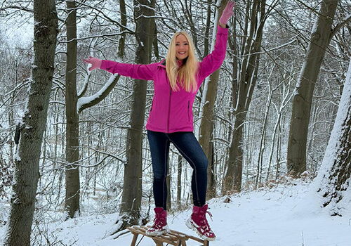 Frau balanciert auf einem Schlitten im verschneiten Wald.