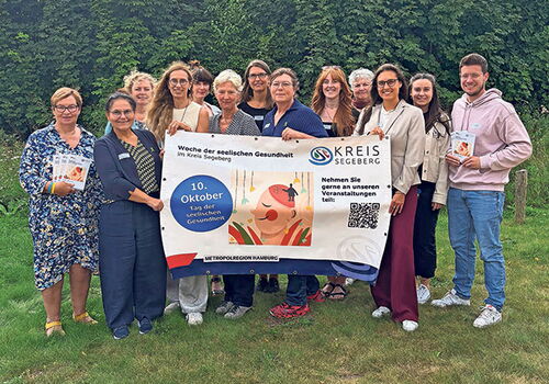 Gruppe posiert mit Banner über seelische Gesundheit im Freien.