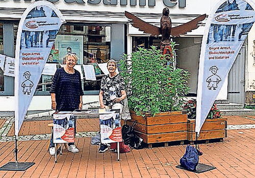 Zwei Frauen an einem Infostand vor einem Geschäft.