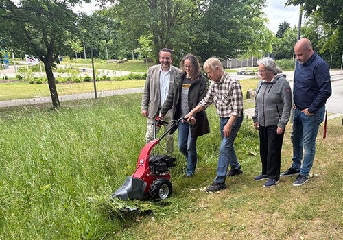 Fünf Personen schauen eine rote Maschine im Gras an.