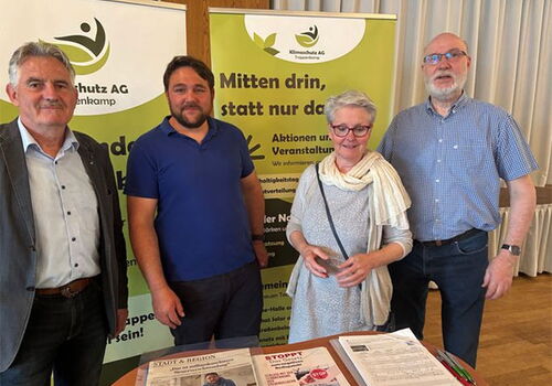 Vier Personen vor zwei Info-Ständen in einem Raum.