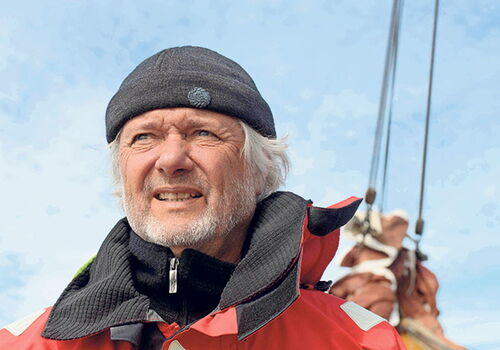 Mann in roter Jacke auf einem Boot, mit blauem Himmel.