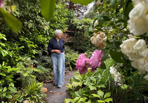 Frau im Garten umgeben von grünen Pflanzen und Blumen.