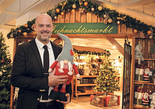 Mann hält Wichtel vor einem Weihnachtsmarkt-Laden.