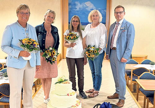 Fünf Personen posieren mit Blumensträußen vor einer großen Torte.