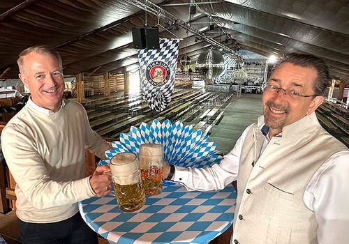 Zwei Männer mit Bierkrügen im leeren Festzelt.