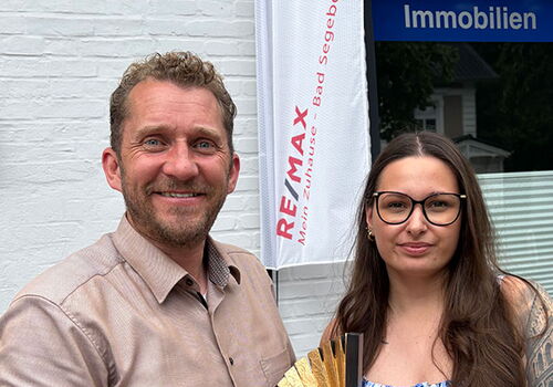 Zwei Personen mit einem Preis bei Remax Immobilien.