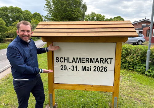 Mann zeigt auf Schild mit Schriftzug 'Schlamermarkt 29.-31. Mai 2026'