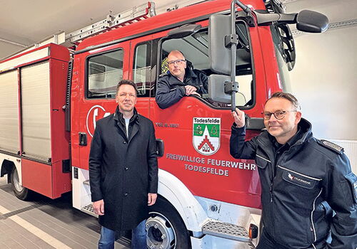 Drei Männer posieren vor einem Feuerwehrauto.