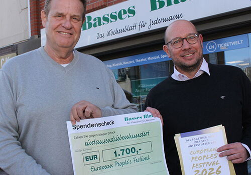 Zwei Männer halten einen Scheck vor einem Bürogebäude.