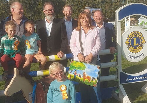 Gruppe von Menschen posiert vor Lions Club Schild im Freien.