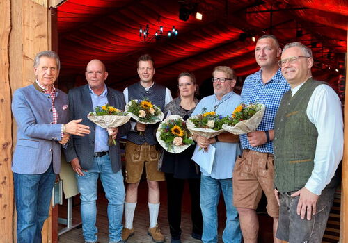 Gruppe von Menschen mit Blumensträußen vor Holzhütte.