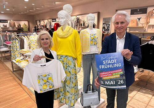 Zwei Menschen in einem Kleidungsgeschäft, sie halten ein Plakat.