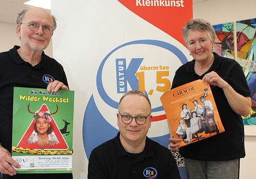 Drei Personen halten Werbeplakate vor einem Banner.