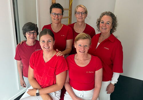 Sechs Frauen in roter Kleidung lächeln in die Kamera.
