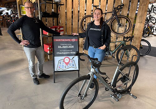 Zwei Personen neben Fahrrad und Ankündigungstafel im Laden.