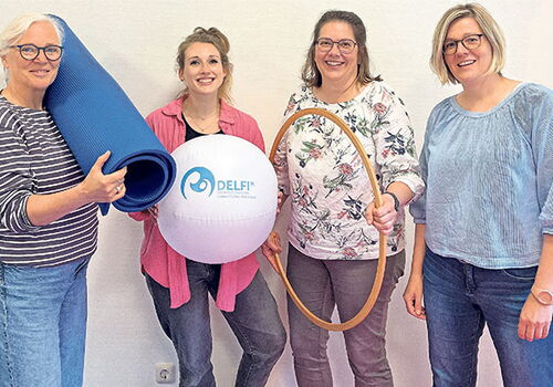 Vier Frauen mit Matten und Sportgerät vor hellem Hintergrund.