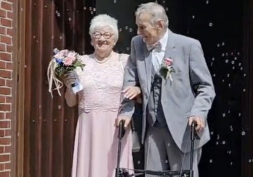 Älteres Paar verlässt die Kirche mit Blumen und Rollator.