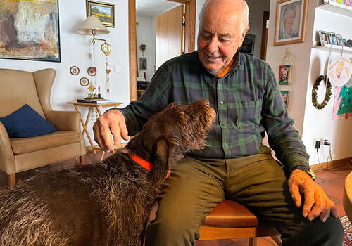 Älterer Mann streichelt einen Hund im Wohnzimmer.